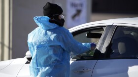 A medical technician performs a nasal swab test on a motorist queued up in a line at a COVID-19 testing site in Colorado.