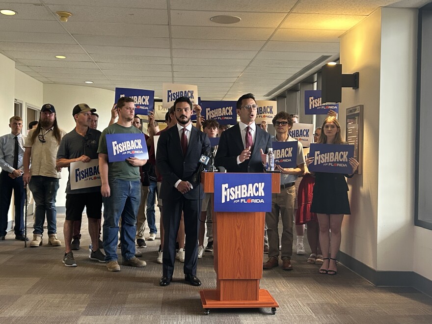 Republican gubernatorial candidate James Fishback speaks at a podium surrounded by supporters and "Fishback for Florida" signs during a news conference inside a government building.