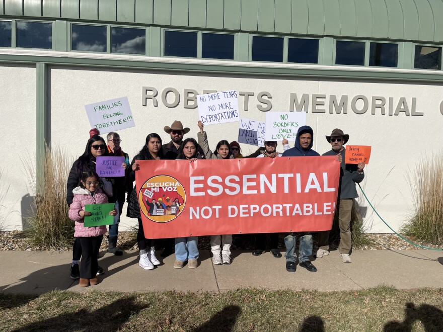 A group of people hold a red sign saying, "essential, not deportable."