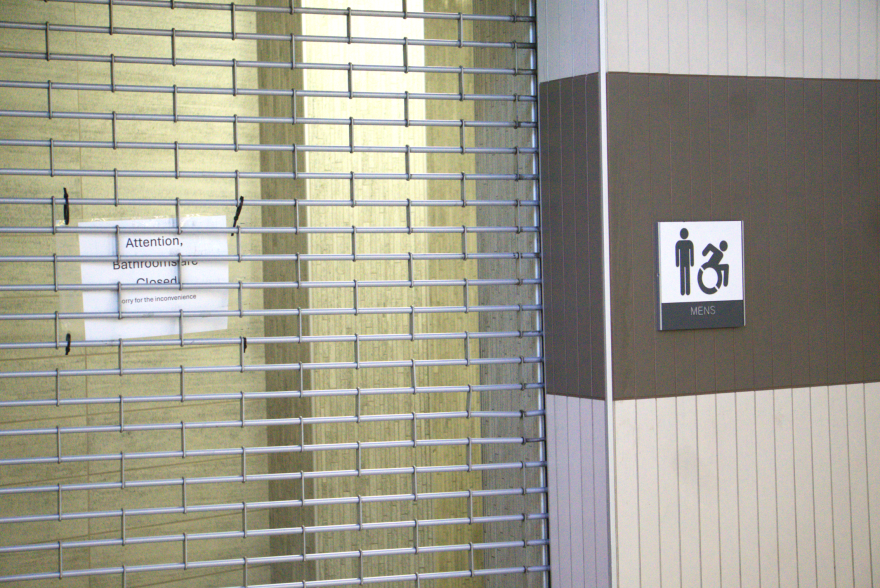 A sign reading, "Attention, Bathrooms are Closed. Sorry for the inconvenience" is attached to the security grille or gate on a recent weekday in March 2026, inside the downtown transit center.