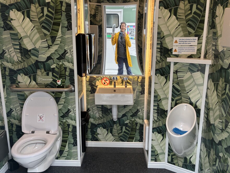 Bathroom selfie! KUOW reporter Anna Boiko-Weyrauch poses with her microphone and commemorates a successful trip to the Throne toilets in Pioneer Square, May 15, 2026. 