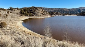 A red body of water with hills and sagebrush around it on a blue sky day. 