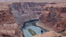 A man looks out over the Colorado River near Page, Ariz.. The seven states that manage the river are divided about how to account for the impacts of climate change in new plans about sharing its water.