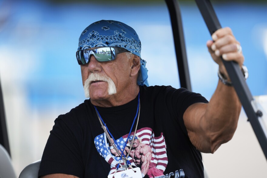 Hulk Hogan is seen with a blue bandana, black T-shirt and sunglasses, sitting in a golf cart