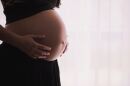 A pregnant woman holds her belly in front of a white curtain backdrop