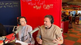 A woman and a man talk in a red diner booth with mics in front of them