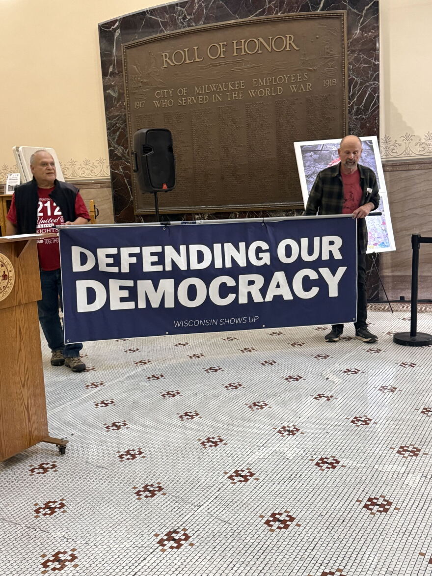 Two men holding a  blue sign that says "Defending our Democracy"