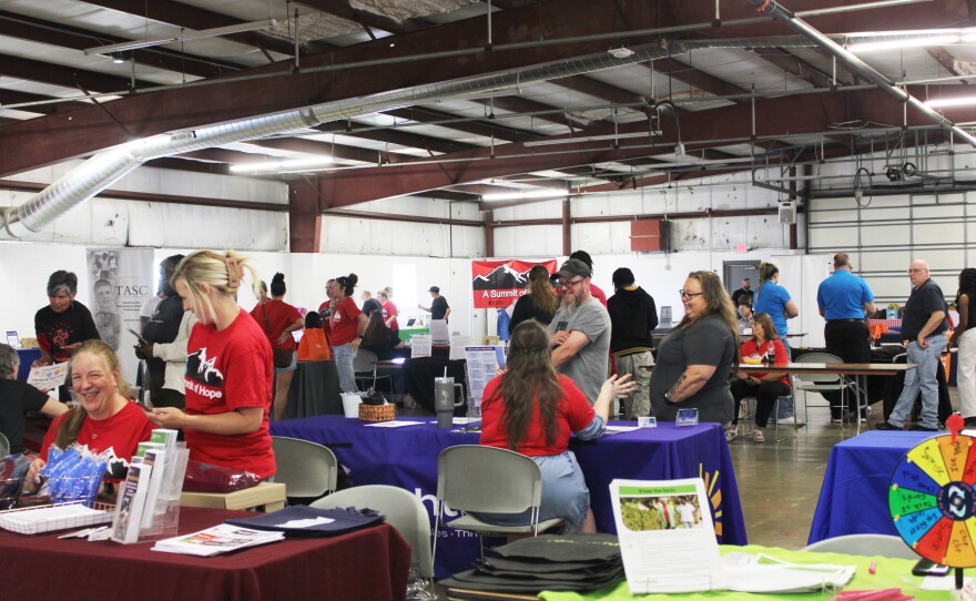 A crowd of people are scattered around a large gathering space with tables and vendors.