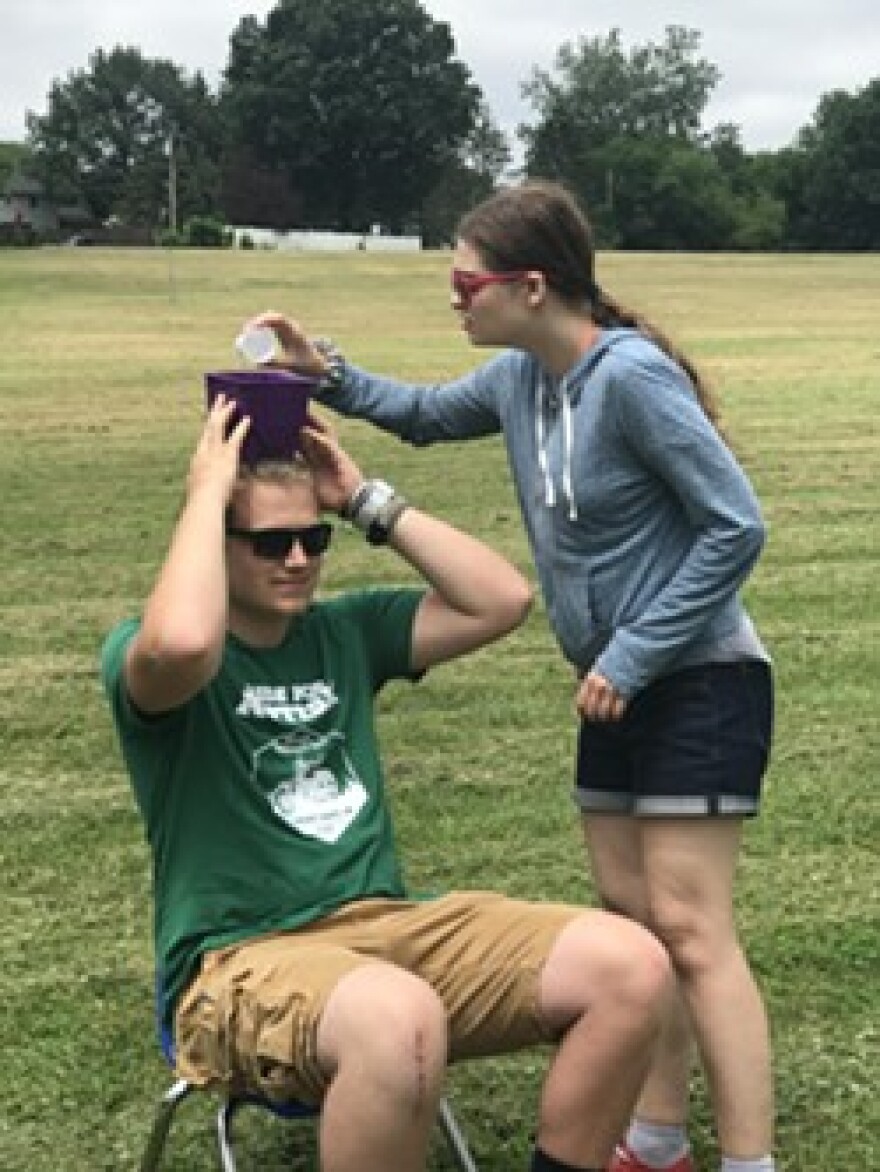 A camper pours water into a bucket on top of a counselor's head in a camp activity in the summer of 2019.