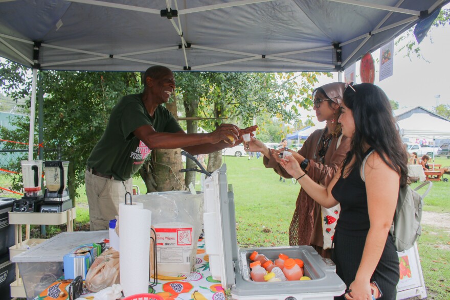 Willie Robinson, owner of Life In A Bottle, serves samples of his pineapple and watermelon smoothies to two new customers from his vendors tent at Gainesville Farmers Market at Heartwood and South Main Station, September 16, 2022. (Ismara Corea/WUFT News)