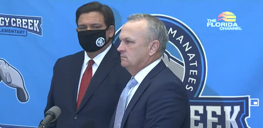 Florida education commissioner Richard Corcoran talks to reporters at a press conference at Boggy Creek Elementary in Kissimmee on Monday November 30th, as Gov. Ron DeSantis looks on. Image: Florida Channel. 