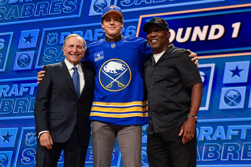 Ilia Morozov, center, stands with NHL Commissioner Gary Bettman, left, and former Buffalo Bills player Thurman Thomas after being drafted by the Buffalo Sabres during the NHL hockey draft Friday, June 26, 2026, in Buffalo, N.Y. (AP Photo/Adrian Kraus)
