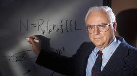 Frank Drake poses in front of white board with the Drake Equation