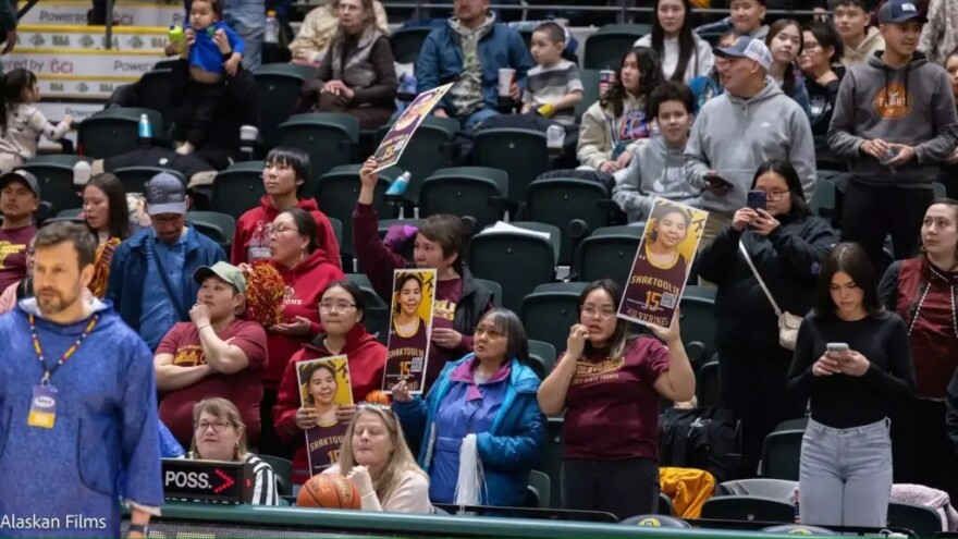 Audience members hold posters with Kelly Hunt's face at the 2026 ASAA State Basketball Championships in Anchorage.