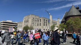 A photo of people carrying signs walking in downtown Greensboro for the city's third No Kings protest.