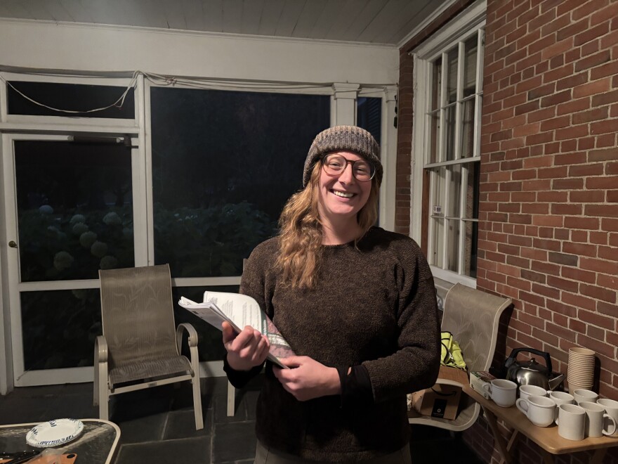 A woman holding papers smiles in front of a brick wall