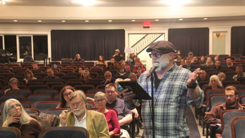 A man speaks into a microphone at a public hearing. 