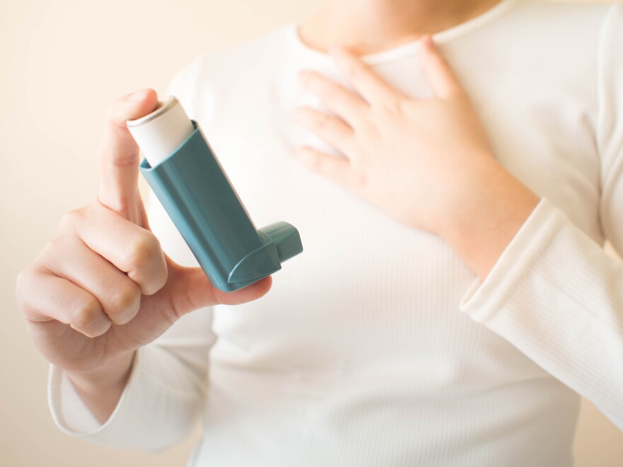 Young female in white t-shirt using blue asthma inhaler for relief asthma attack. Pharmaceutical products is used to prevent and treat wheezing and shortness of breath caused asthma or COPD. Close