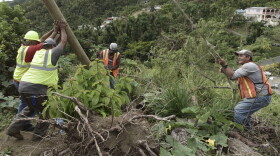 In this Jan. 31, 2018 photo, Public Works Sub-Director Ramon Mendez, wearing a hard hat at left, works with locals who are municipal workers, from right, Eliezer Nazario, Tomas Martinez and Angel Diaz as they install a new post to return electricity to Felipe Rodriguez's home, four months after Hurricane Maria hit the El Ortiz sector of Coamo, Puerto Rico. Coamo's city government relies on residents to tell it where damaged cables and posts are located, and uses hand-drawn maps to show homes that have power or need it, and the city updates the power company. (Carlos Giusti/AP)