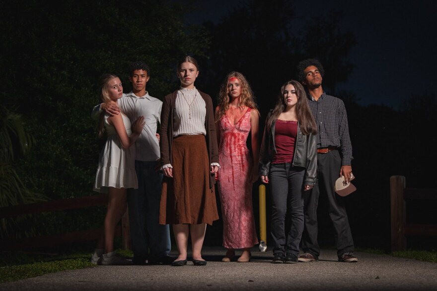 Cast of actors in costume standing outside looking grim at the camera 