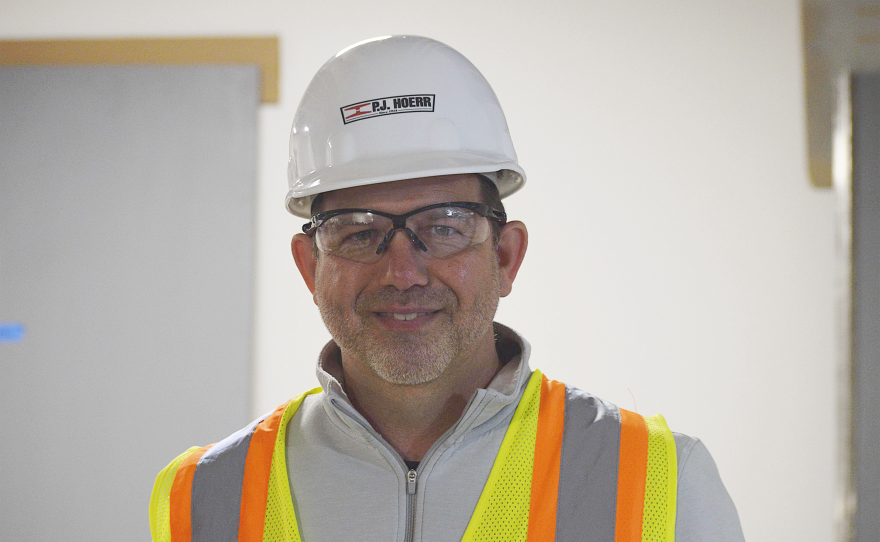 Man in hard hat and hi-vis vest smiles.