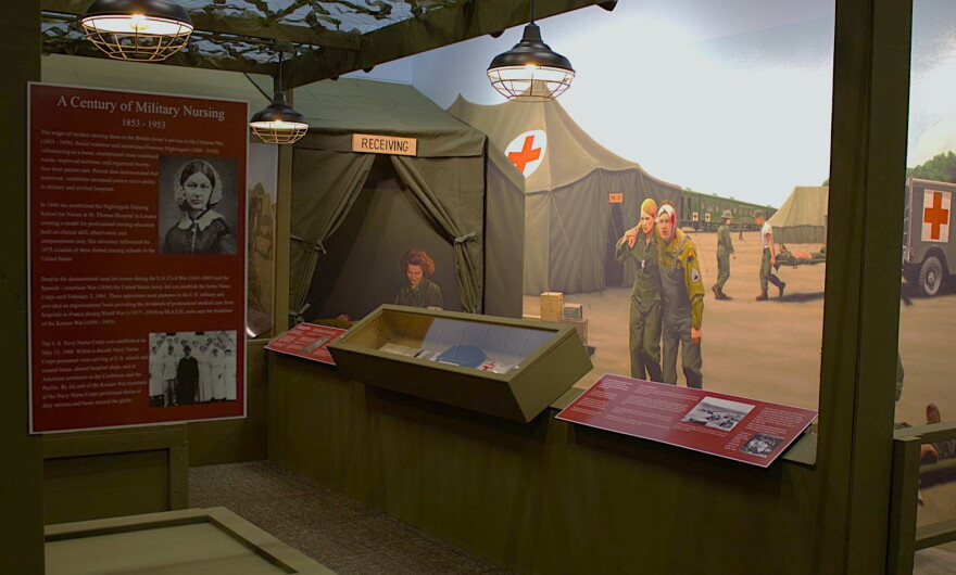 A wall mural of military nurses helping injured soldiers at a real evacuation hospital from WWII can be seen behind displays of Iowa nurses' stories and artifacts.