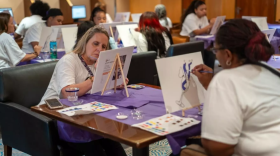 Un grupo de mujeres se sienta alrededor de mesas rectangulares para pintar en pequeños caballetes de mesa durante el crucero de sobrevivientes de violencia doméstica del año pasado.