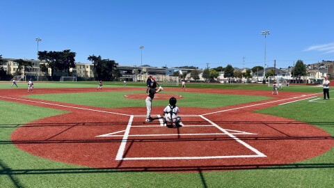 A baseball field where a girl in a black shirt and white pants gets ready to hit a baseball with her bat