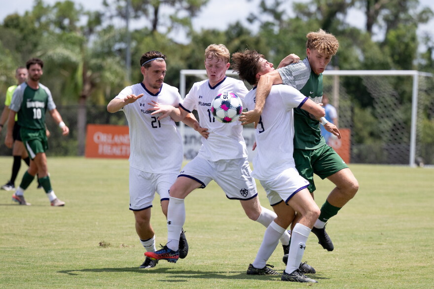 3 soccer players in white uniforms compete with a player in green for a loose ball