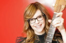 Woman with reddish blonde hair holding up a guitar 