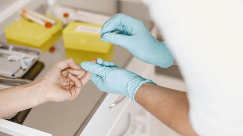 A nurse taking a blood sample from a finger.