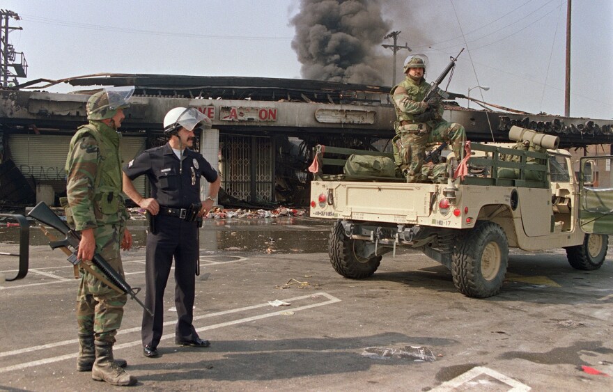 National Guardsmen and a police officer take up security positions in front of a burned and looted shopping center, May 1, 1992, in central Los Angeles.