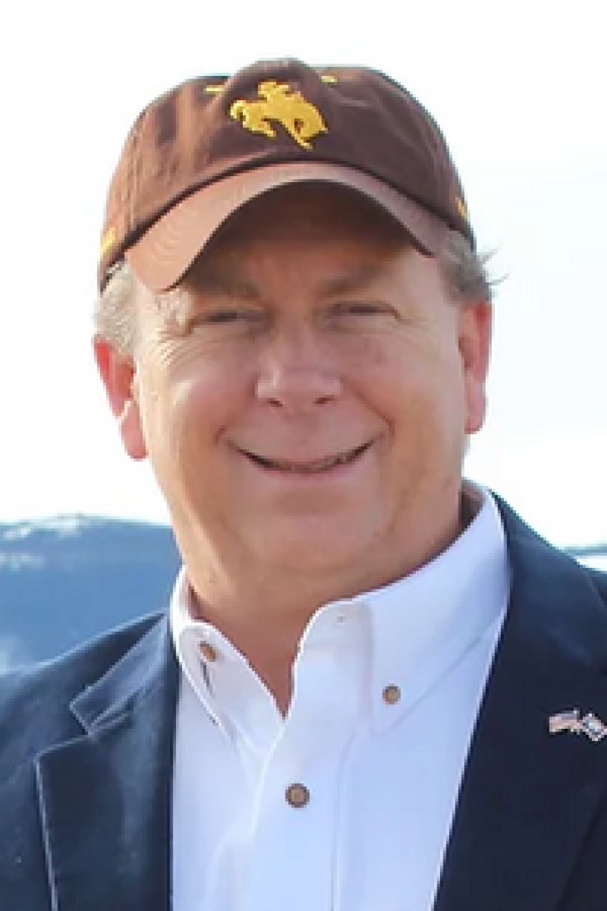 Older man smiling in baseball cap, white button down shirt and black jacket