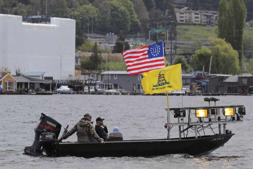 Protesters fly a "Don't Tread on Me" Gadsden flag and a flag representing the conservative Three Percenters group as they sit on a boat on Lake Union near Gas Works Park in Seattle, Sunday, April 26, 2020.