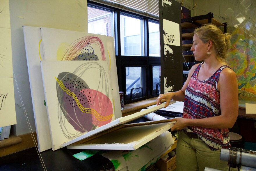 A woman looks at canvases filled with oval shapes.