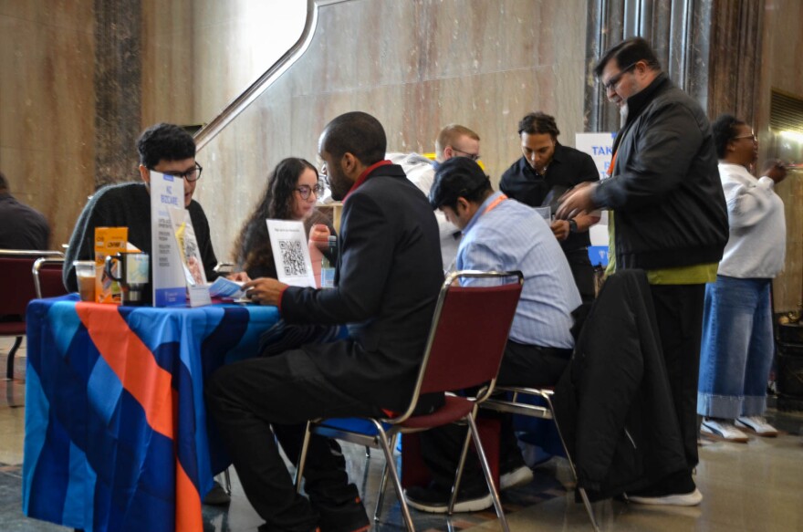 People sit around a tablecloth that is blue and red looking over documents and computers. 