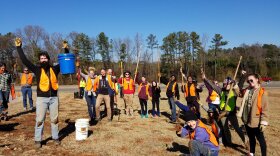 A crowd of volunteers wearing safety vests, hoisting their shovels and buckets up in the air in celebration outside at a site for the Martin Luther King Jr. Day of Service in 2023