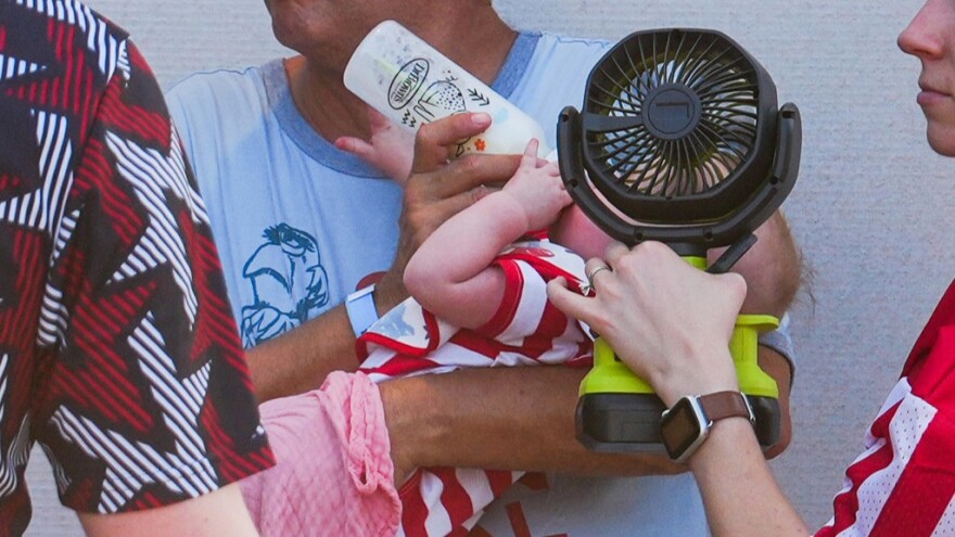 A woman holds a fan in front of a bottle-fed baby at the Great American State Fair during an extreme heat wave, Friday, July 3, 2026, on the National Mall in Washington.