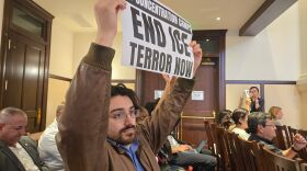 A protester holds up a sign at Bexar County Commissioners Court, March 10, 2026