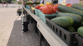 Table with many baskets of vegetables under a tent next to some flowers