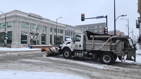 A City of Columbia snowplow makes its way through the intersection of Ninth Street and Broadway in downtown Columbia. The snow on the road is mostly white, but browning and turning to slush. Tire tracks in the snow are visible.