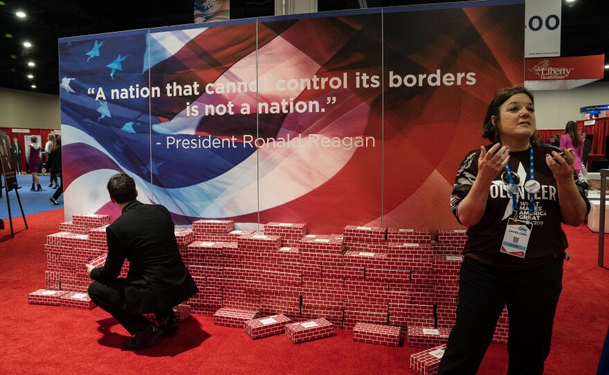 A fake wall, made of cardboard bricks, is on display with a quote by former President Ronald Reagan that reads: "A nation that cannot control its borders is not a nation."