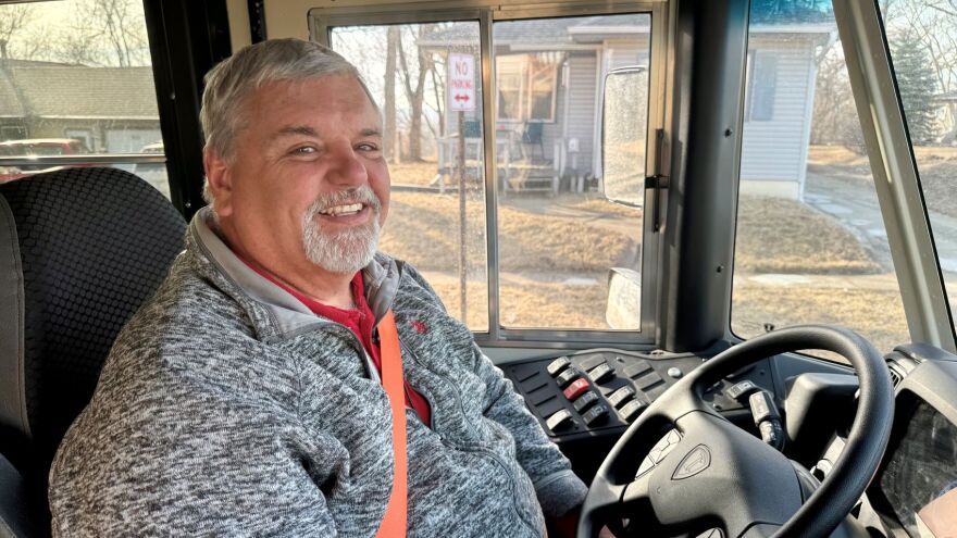 A bus driver is sitting behind the wheel and smiling.