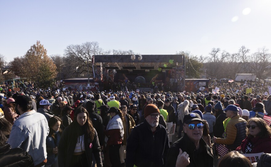 A large crowd is seen outside with a covered stage in the background. 