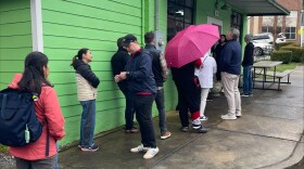 A line of customers stand outside of a green building.