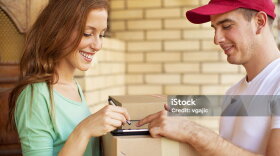 Delivery man delivering packages to female customer at house door. Young woman smiling and signing digital receipt on a digital tablet.