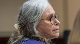 A woman with grey hair and a purple jumpsuit listens to statements made on her behalf by family friends during her sentencing for her role in the murder of Dan Markel.