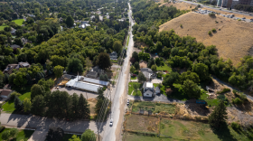 Aerial view of part of Logan. A road cuts through the trees of a neighborhood, up against a hill that leads to campus buildings.