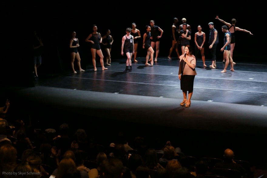 woman stands on stage with dancers in background