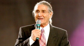 man in dark suit talks behind a podium with a microphone